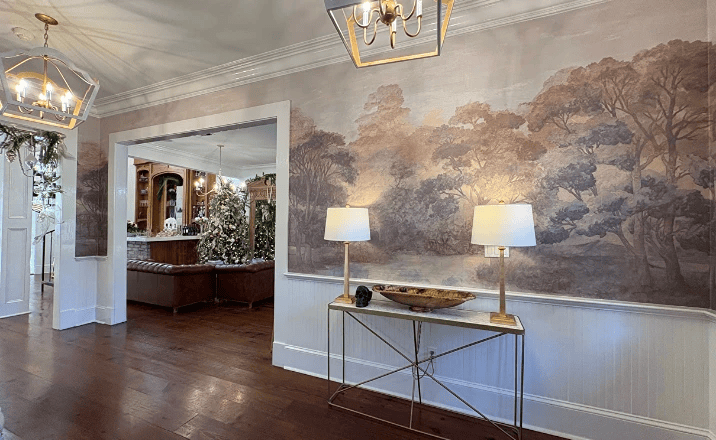 Wallpaper with a landscape scene above wainscoting, paired with a console table and festive room view.